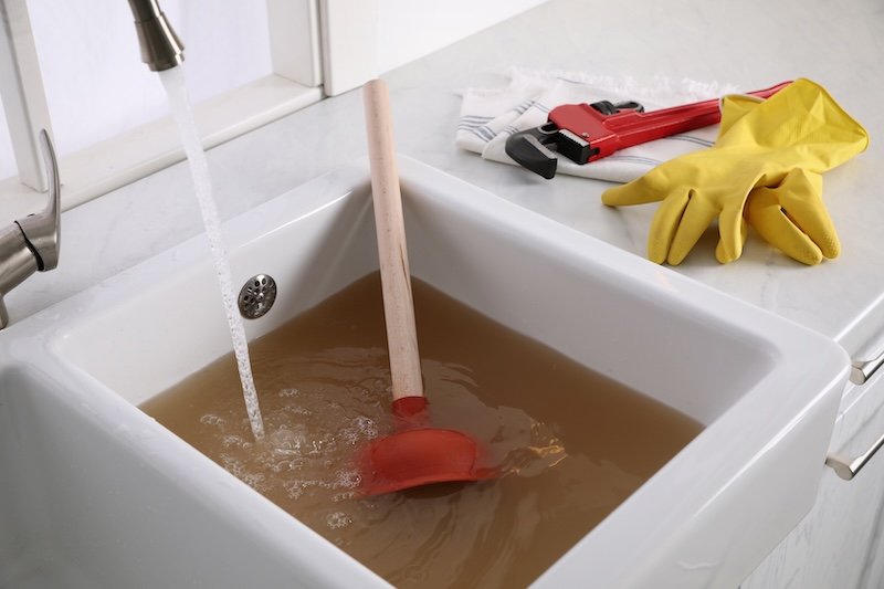 Kitchen counter with clogged sink, plunger and plumber's accessories sewer line issue