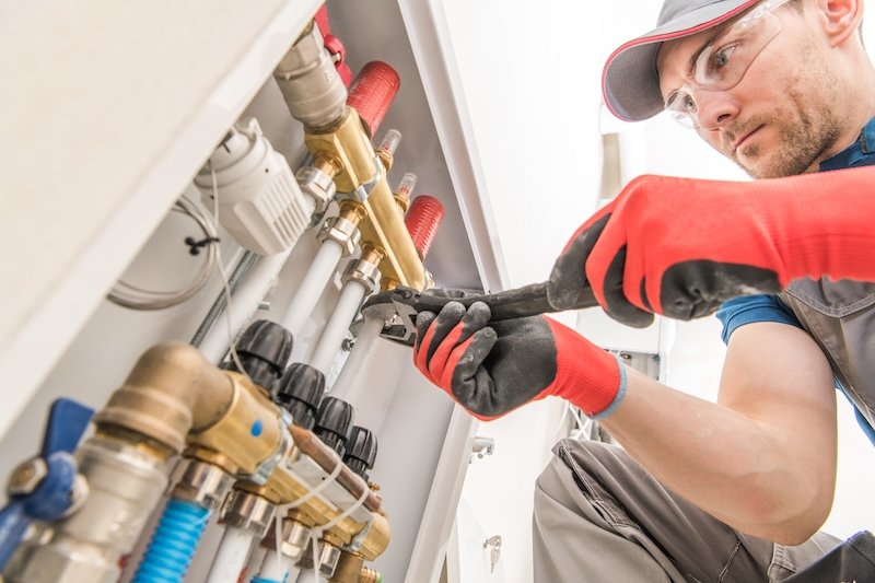 Residential House Floor Heating Valves Adjustment. Plumbing and Heating Technician at Work.