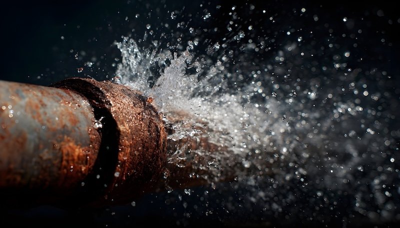 A rusty pipe bursts spraying water in a dramatic urgent scene highlighting a plumbing emergency and potential damage