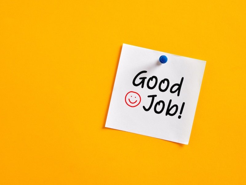 Handwritten word good job on a note paper pinned on a yellow board. Appreciation or congratulating an achievement in business.