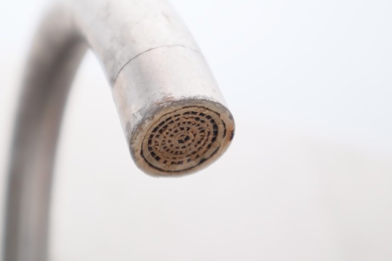Extreme close-up of a metal tap nozzle showing heavy calcium buildup and rust on the aerator. A concept of hard water damage, poor water quality, and plumbing maintenance needs