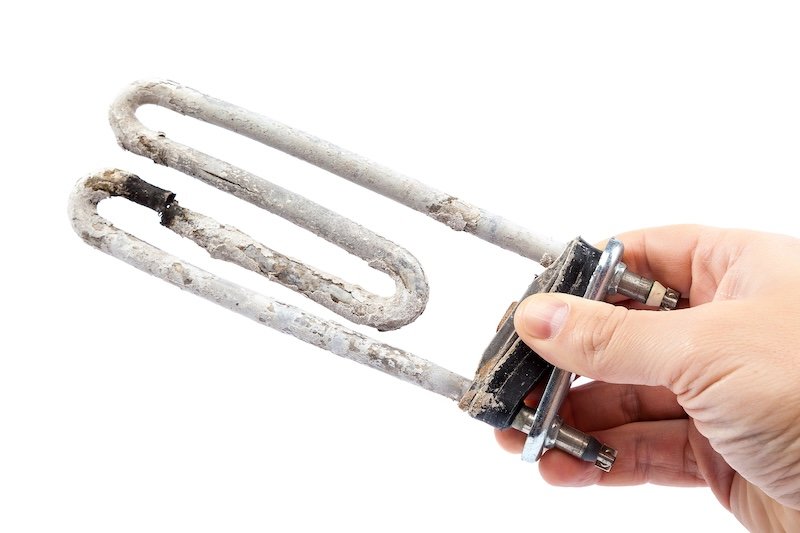 Damaged heating element of the washing machine in a hand on a white background.