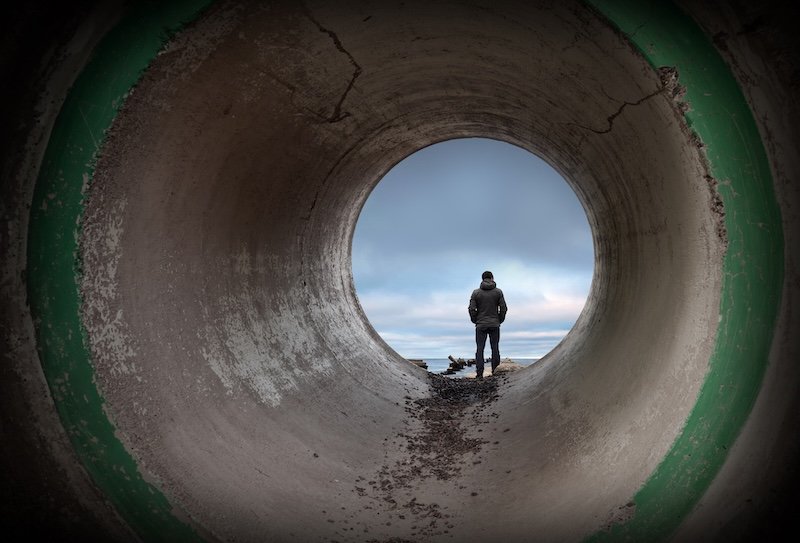 Man looks at horizon in the end of dark concrete tunnel