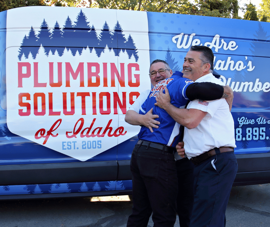 Plumbing Solutions of Idaho plumbers hugging each other on national hug a plumber day in front of work van
