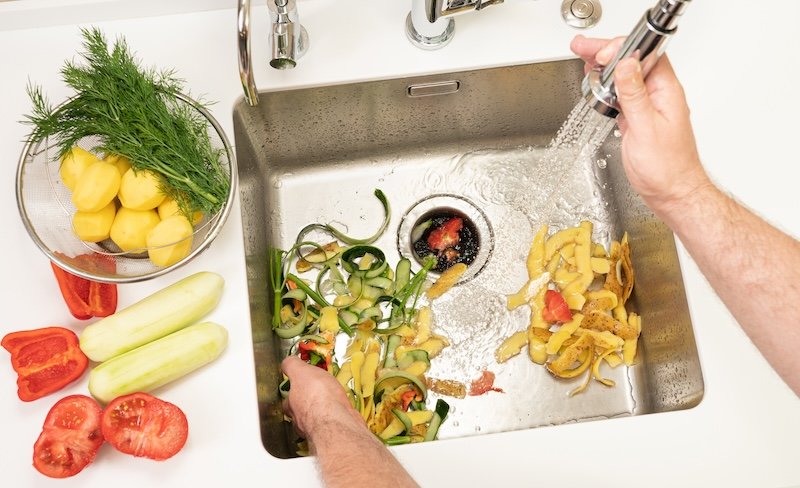 A man recycles food waste using a modern kitchen disposer. garbage disposals