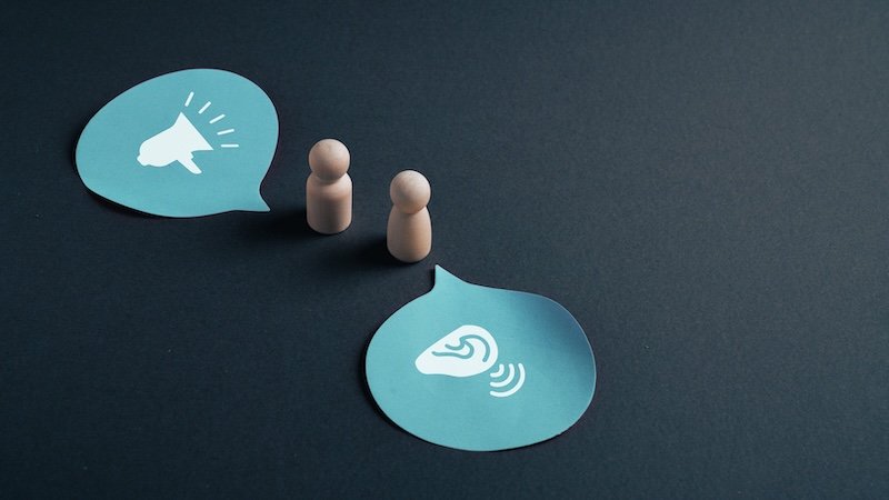 Concept of active listening and effective communication between two wooden figures represented by megaphone and ear symbols inside speech bubbles, idea of dialogue, understanding and assertive business conversation.