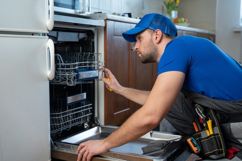 Repair of dishwashers. Repairman repairing dishwasher in kitchen.