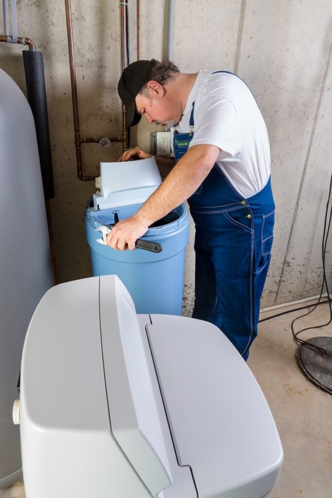 Workman installing a domestic water softener troubleshooting installation problems in a basement utility room