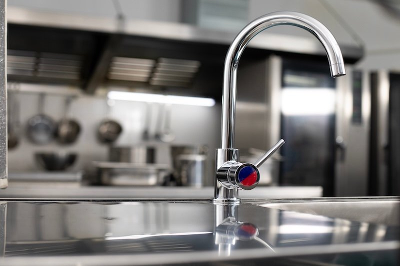 Metal faucet in a big professional restaurant kitchen, close up. Red and blue, hot and cold water mixer