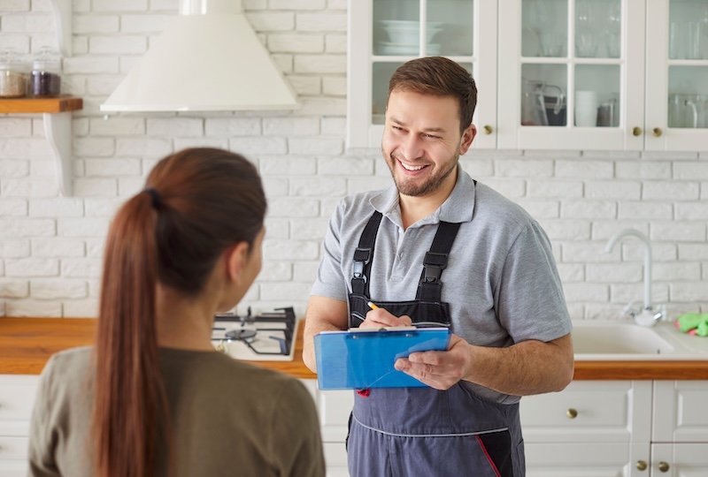 Man plumber talking with female client signing contract for plumbing services at home. Male mechanic or repairman consulting woman customer standing in kitchen. Maintenance and repair service for plumbing maintenance