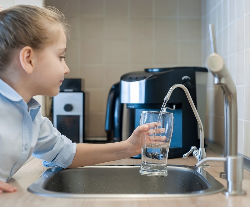 Child pouring fresh reverse osmosis purified water in kitchen at home. Drinking tap water. Consumption of tap water contributes to the saving of water in plastic bottles. Protection of the environment