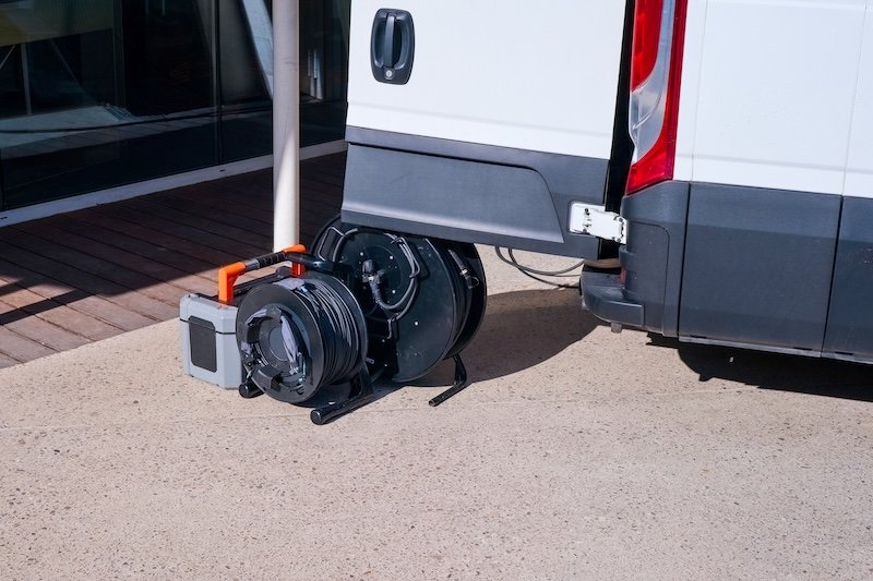 Professional sewer camera reel and inspection system next to a service van. CCTV pipe inspection equipment for plumbing and drainage diagnostics on city street. Industrial maintenance concept.