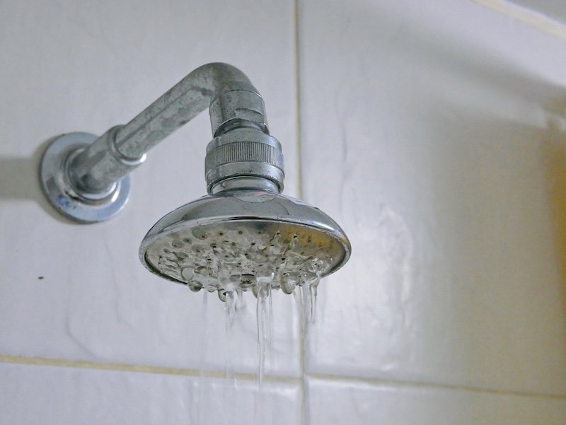 Close up of a partly clogged shower head in a bathroom, causing it to putting out so little water