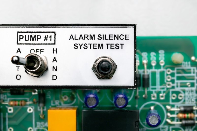Pump  controller or pump system control panel, close up. Used in residential or commercial sump and sewage system. Focus on the alarm silence test switch with defocused motherboard. Selective focus.