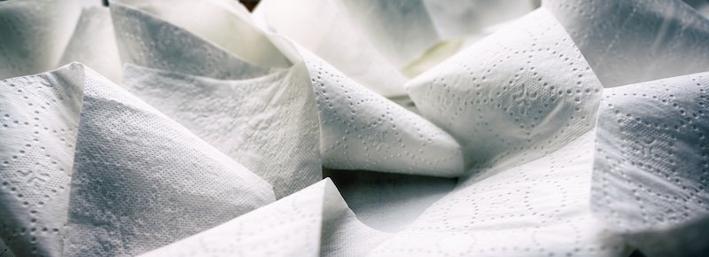 Close-up at folded unrolled white toilet paper. Banner proportioned high resolution image.
