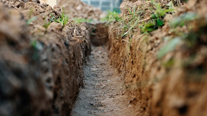 Dig a trench. Earthworks, digging trench. Long earthen trench dug to lay pipe or optical fiber. Construction the sewage and drainage. View from the trench. Clay soil. Part of the image is blurred